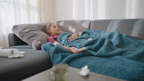 little girl sleeping on couch covered with a cozy blanket, looking peaceful and calm, with tissue paper scattered around and a glass cup on the table