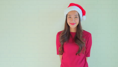 young adult asian woman with red and white christmas bobcap lomg brown hair and t-shirt posing and smiling towards camera