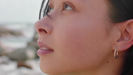 portrait of beautiful asian woman smiling enjoying cloudy seaside exploring vacation lifestyle with wind blowing hair on beach