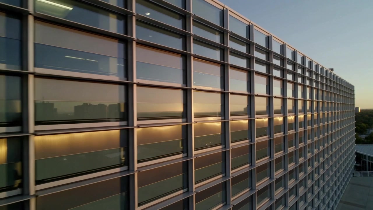 Lanzando una cámara de dron deslizándose a lo largo de los marcos de la fachada de la oficina al atardecer, capturando el disco solar cambiante.
