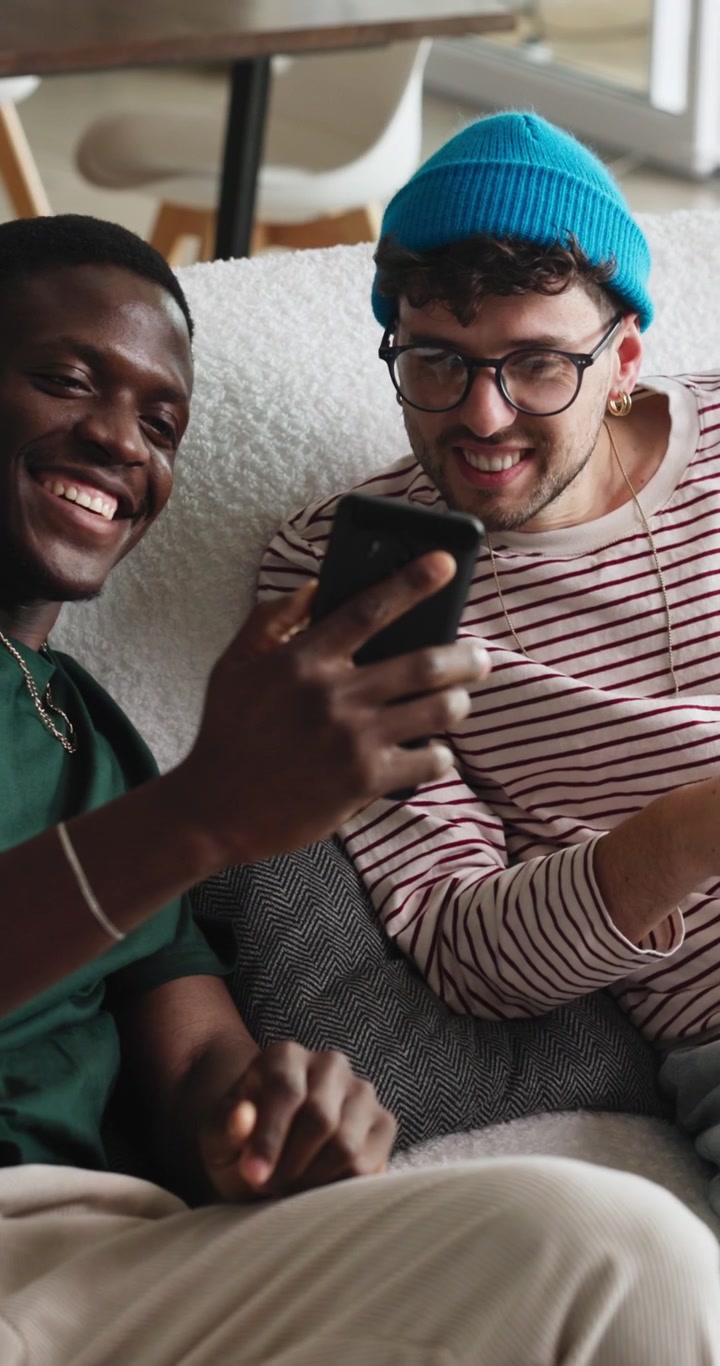 Two Young Men Laughing While Looking at a Smartphone on a Sofa