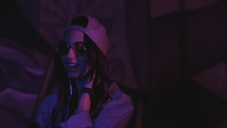 close-up view of teenager caucasian girl wearing glasses and cap with headphones while listening to the music and dancing outdoors at night