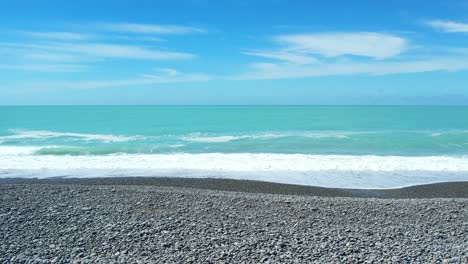 Low aerial slow-motion of small waves breaking onto stony beach at Canterbury Bight - beautiful turquoise-colored South Pacific Ocean
