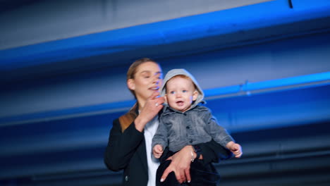 adorable kid sits at the feet of a blond long-haired woman. mother takes her son in hands and turns around with him. low angle view.