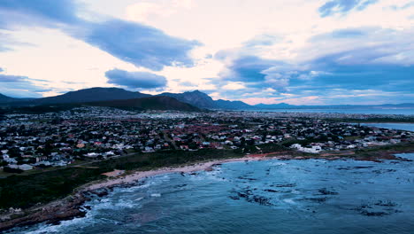 Drone-pullback-over-ocean-view-over-coastal-town-Sandbaai,-moody-cloudscape