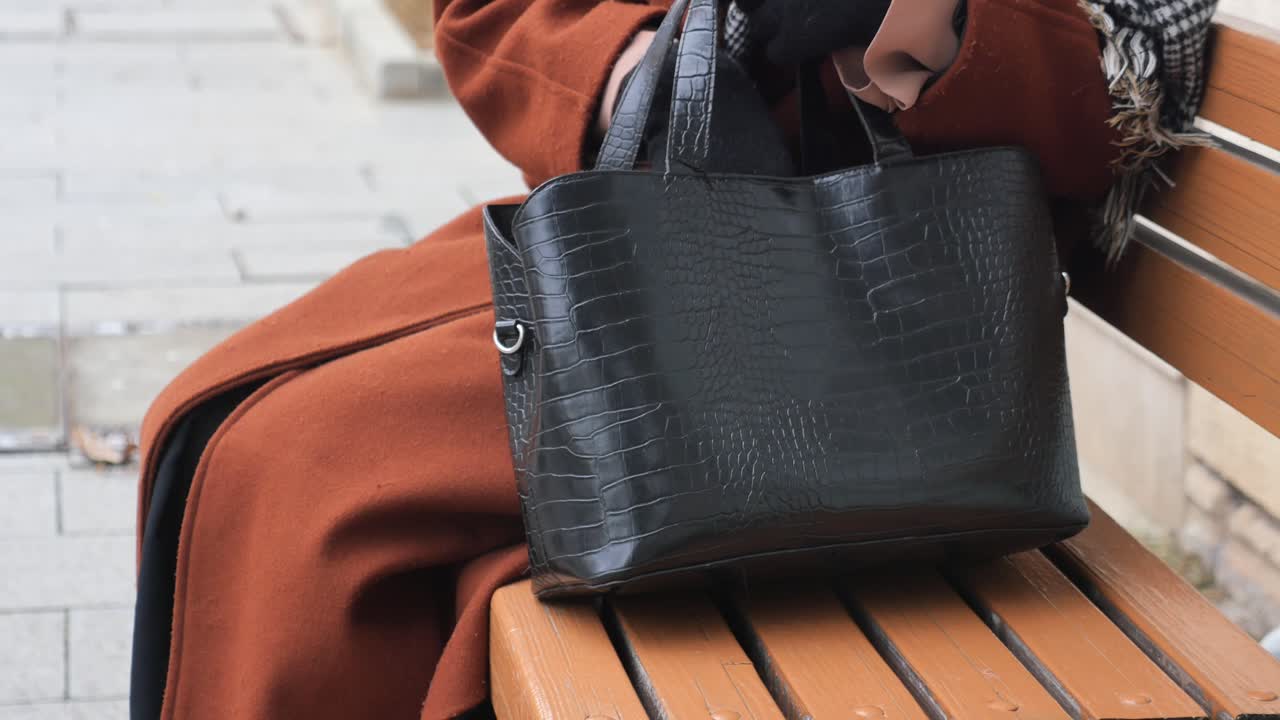 женщина сидит на скамейке с черной кожаной сумочкой