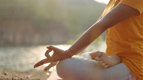 crop view of a woman sitting in padmasana pose during sunrise near a lake.