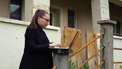 Eine-Junge-Frau-Arbeitet-An-Einem-Laptop-In-Der-Nähe-Eines-Alten-Hauses