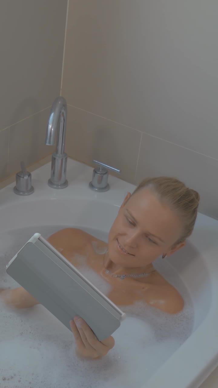 Woman Relaxing in Bubble Bath While Using a Tablet