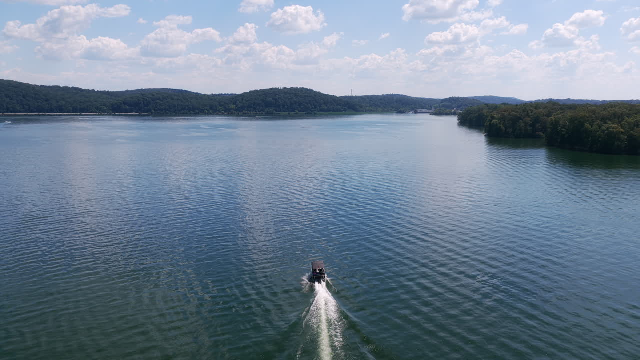 Ripresa aerea di una barca che naviga nelle acque calme di Harrison Bay, circondata da colline boscose e cieli estivi azzurri