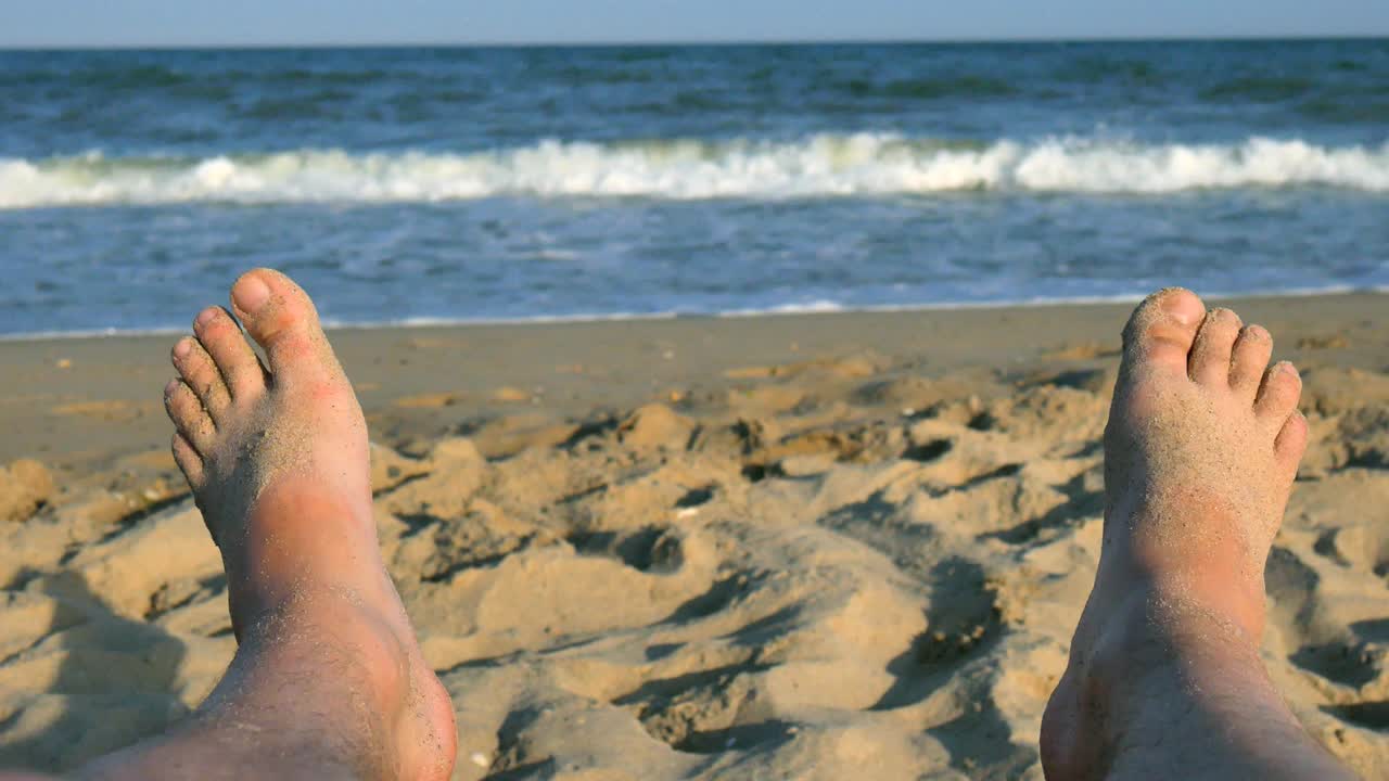 pies de hombre tomando el sol en la playa contra el fondo de arena y mar azul con olas, hombres descalzos en una playa