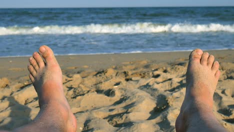 man feet sunbathing on the beach against the background of sand and blue sea with waves, man bare feet on a beach