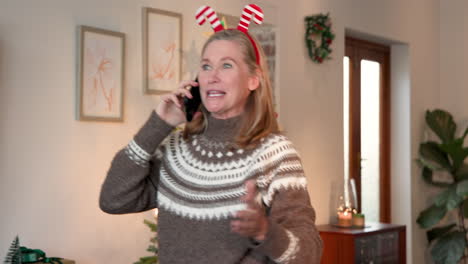 senior woman wearing festive headband talking on phone near christmas tree