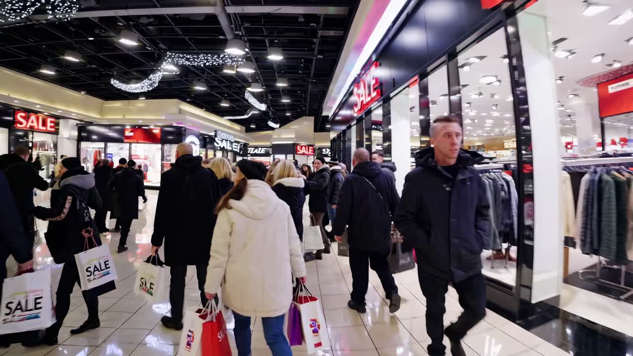 Inquadratura grandangolare di un centro commerciale affollato durante i saldi, che ritrae acquirenti con borse.