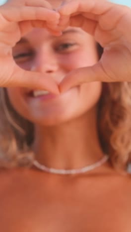 joyful girl expresses love with heart gesture against bright sky