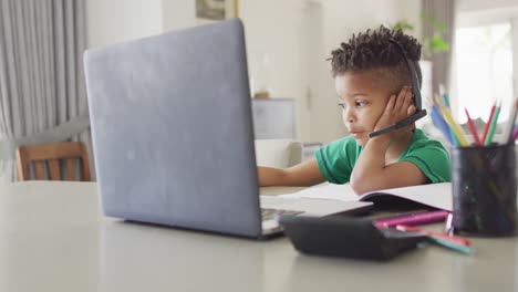 happy african american boy sitting at table, using laptop for online lesson