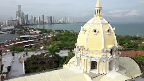old town cartagena fly over aerial cinematic shot showcasing san pedro claver church with modern buildings in bocagrande as backdrop