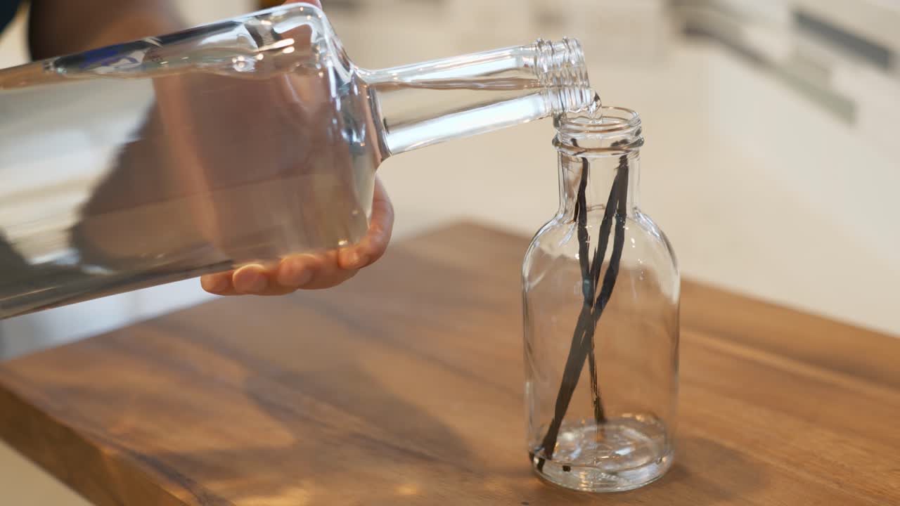 Hand pouring vodka into a glass jar with three vanilla beans it it to make homemade vanilla
