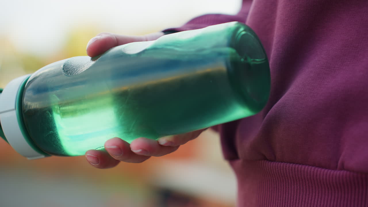 Close up athlete hand gripping translucent green water bottle with visible swirl and condensation motion on blurred outdoor urban background conveying dynamic hydration and fitness energy