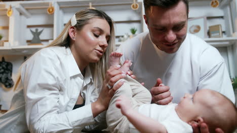 loving mom holding the legs of her newborn and kissing tiny feet. dad holding the son under the head and by the hand.