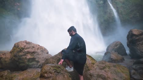 young male walking toward rugged waterfall climbing a rock , wide shot, dolly in