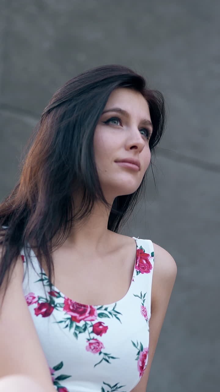 close round motion young pretty woman in dress with flower images fixes hair against huge gray building