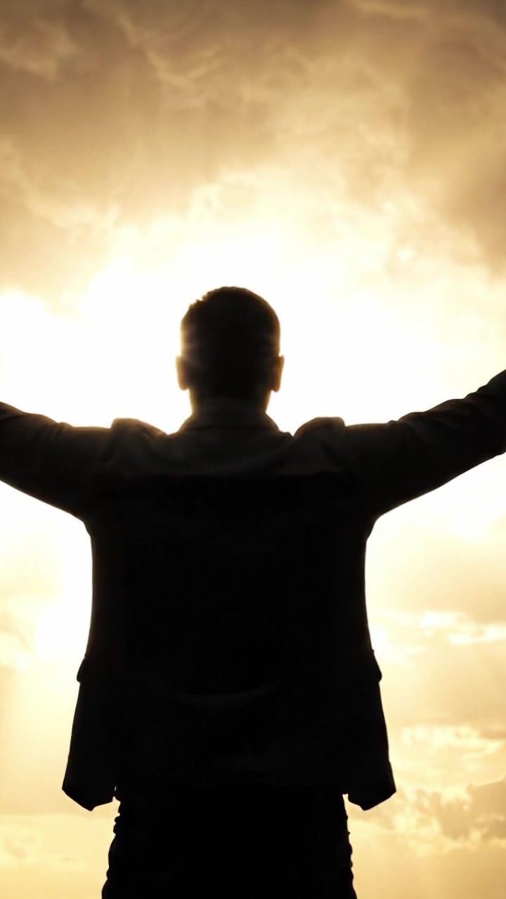Una figura si staglia in silhouette contro un brillante tramonto dorato, con le braccia tese, catturando un momento di libertà e ispirazione sotto cieli drammatici