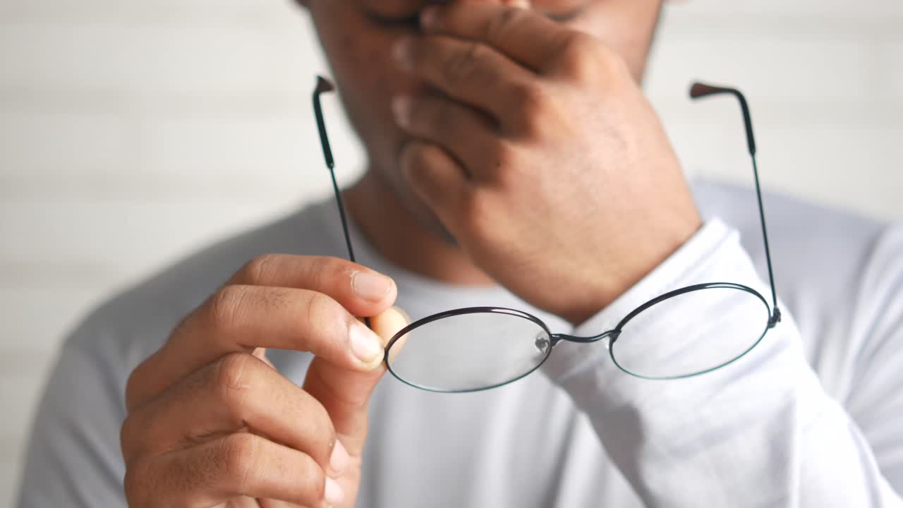 hombre cubriendo la boca con las manos mientras sostiene gafas