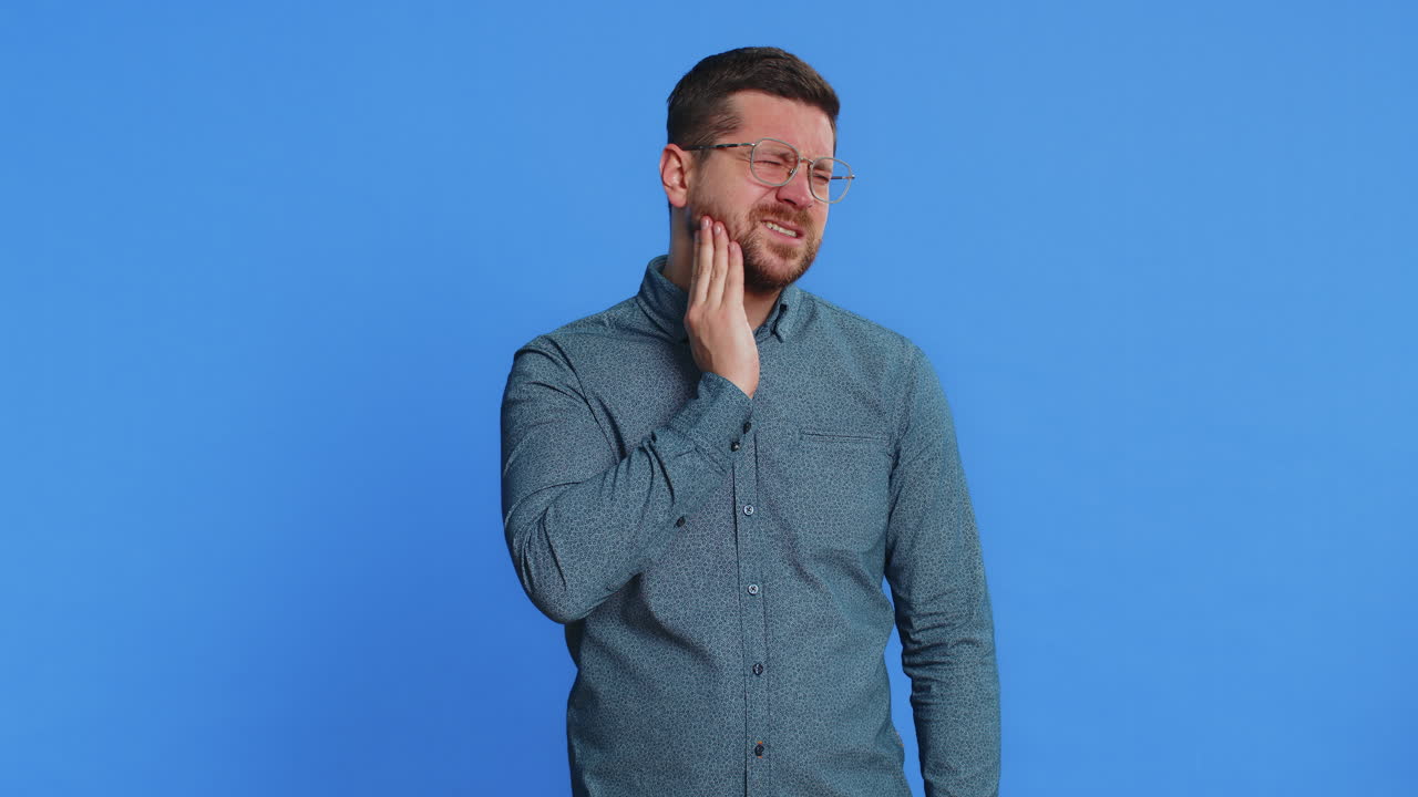 Man in glasses touching cheek closing eyes with expression of terrible suffer from painful toothache