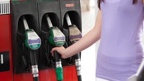 sección media de una mujer caucásica en top lila usando una bomba de combustible en una gasolinera