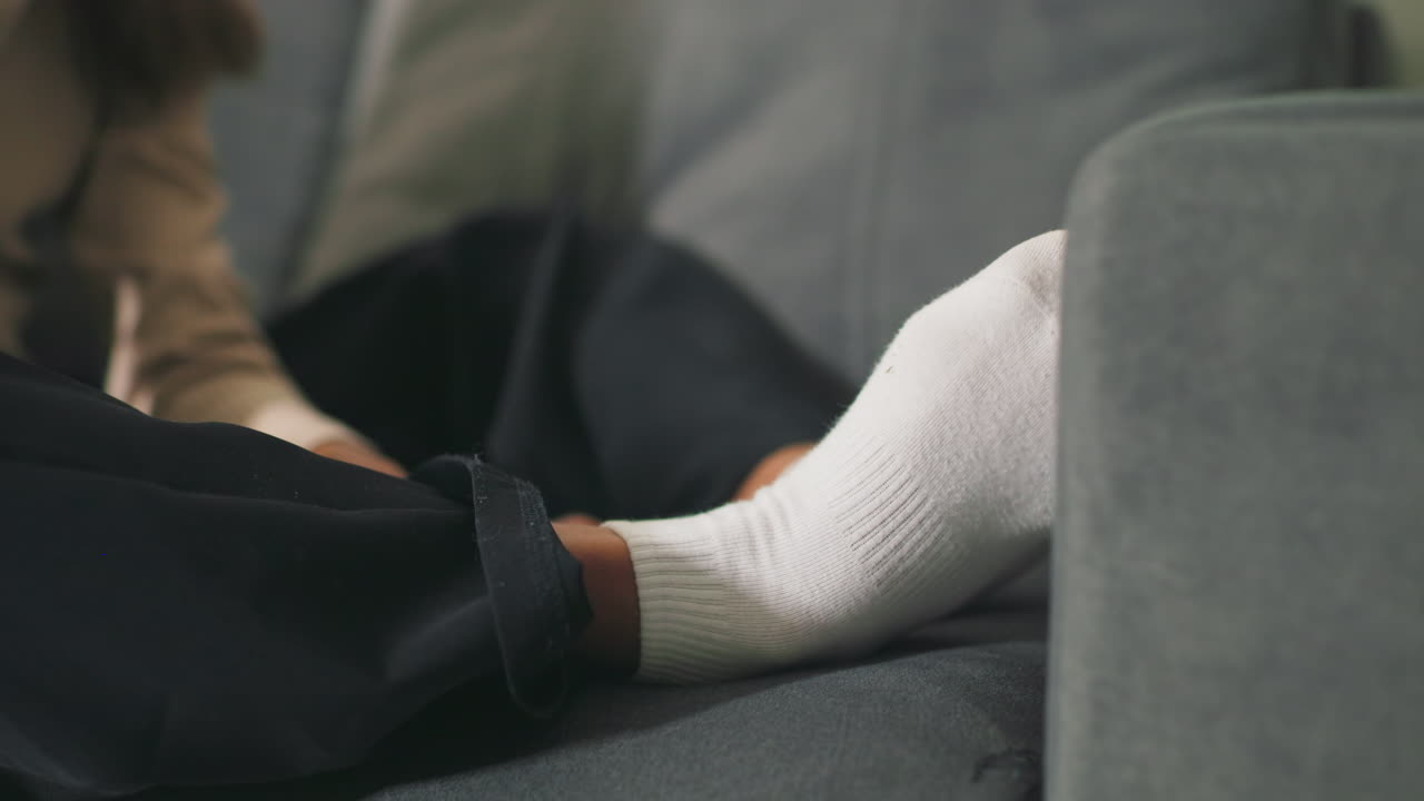 Close-up of girl’s feet in white socks resting on couch. Cozy indoor moment, relaxed posture, focusing on comfort and calm at home, creating peaceful, domestic atmosphere