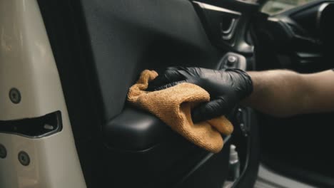 Close-up-of-a-male-wearing-black-gloves-cleaning-a-white-car-with-black-interior-with-a-microfiber-cloth-in-slow-motion