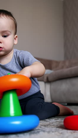 caucasian child collects the colorful rings of toy pyramid. baby learns colors. low angle view. vertical video