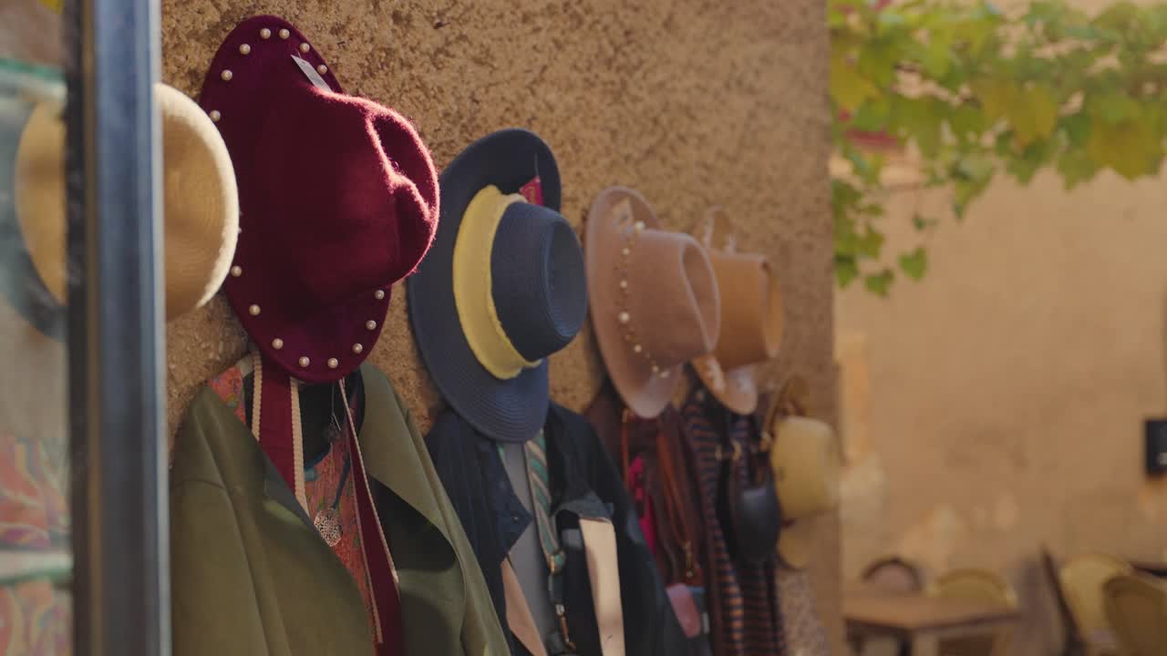 Cappelli e vestiti appesi all'esterno di un negozio boutique di abbigliamento vintage e di seconda mano di stilisti. Un venditore chic da mercatino delle pulci in una città o cittadina europea. Area commerciale turistica. Abbigliamento alla moda nuovo e di tendenza.