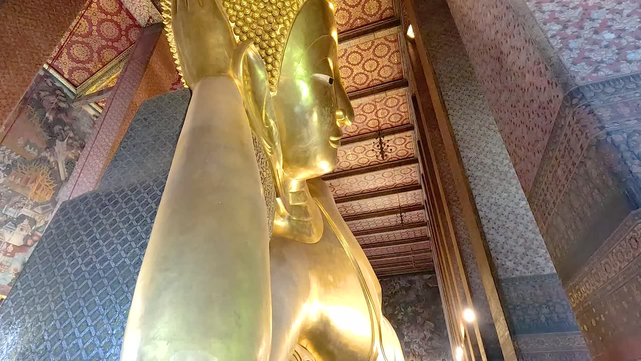 una vista serena de la estatua dorada de buda reclinada en wat pho, bangkok, que muestra detalles intrincados del templo y la iluminación ambiental