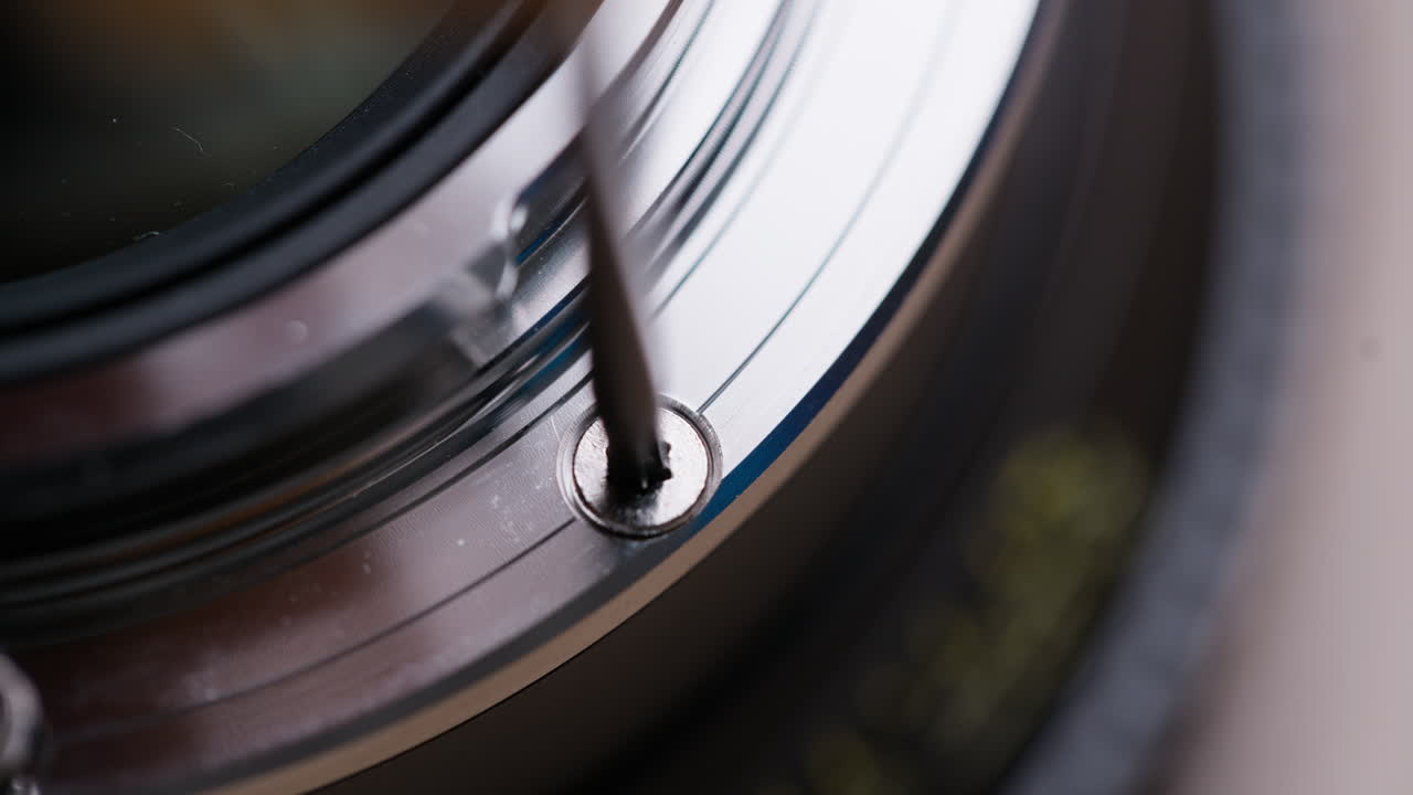Extreme macro close-up of a Torx screw being removed from a cinema lens mount during EF to PL conversion. Screw head and tool clearly visible. Highly detailed technical footage