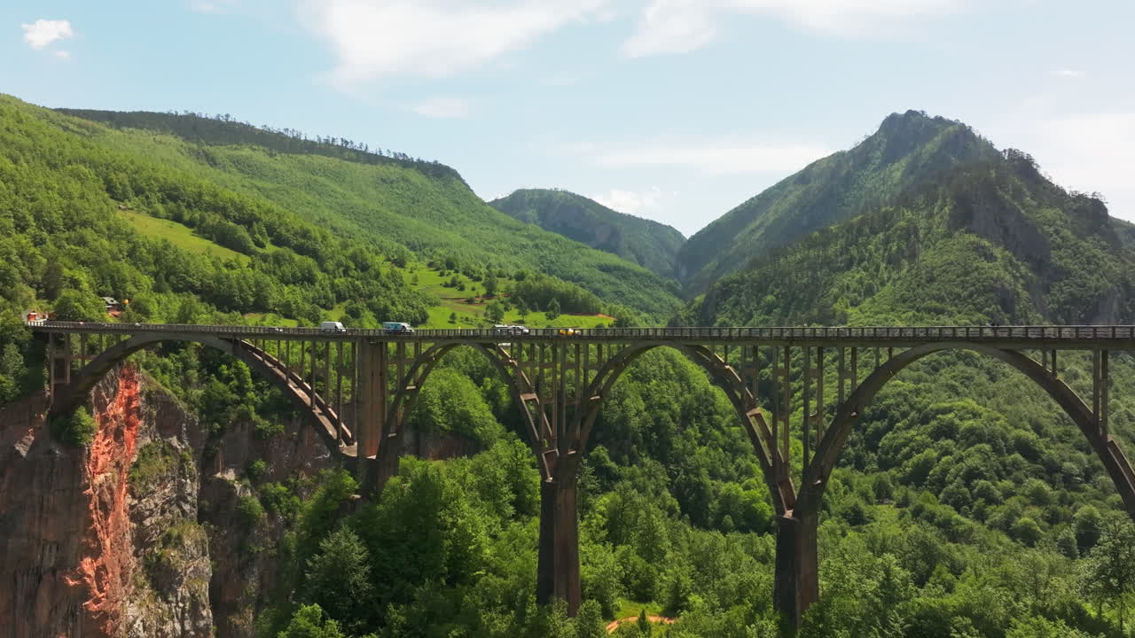 Cars drive over Tara UNESCO arch bridge canyon in lush wilderness; drone