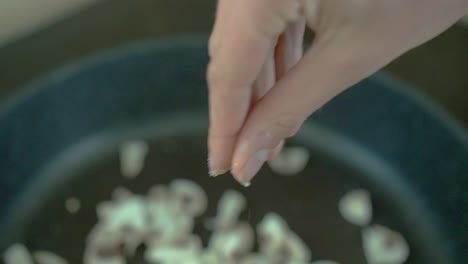 hembra blanca agregando sal a los champiñones en una sartén