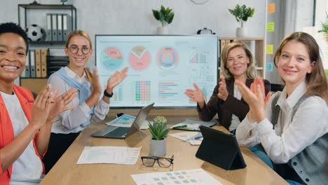 success and luck concept where attractive happy smiling experienced multiethnic group of businesswomen clapping hands during joint meeting in office