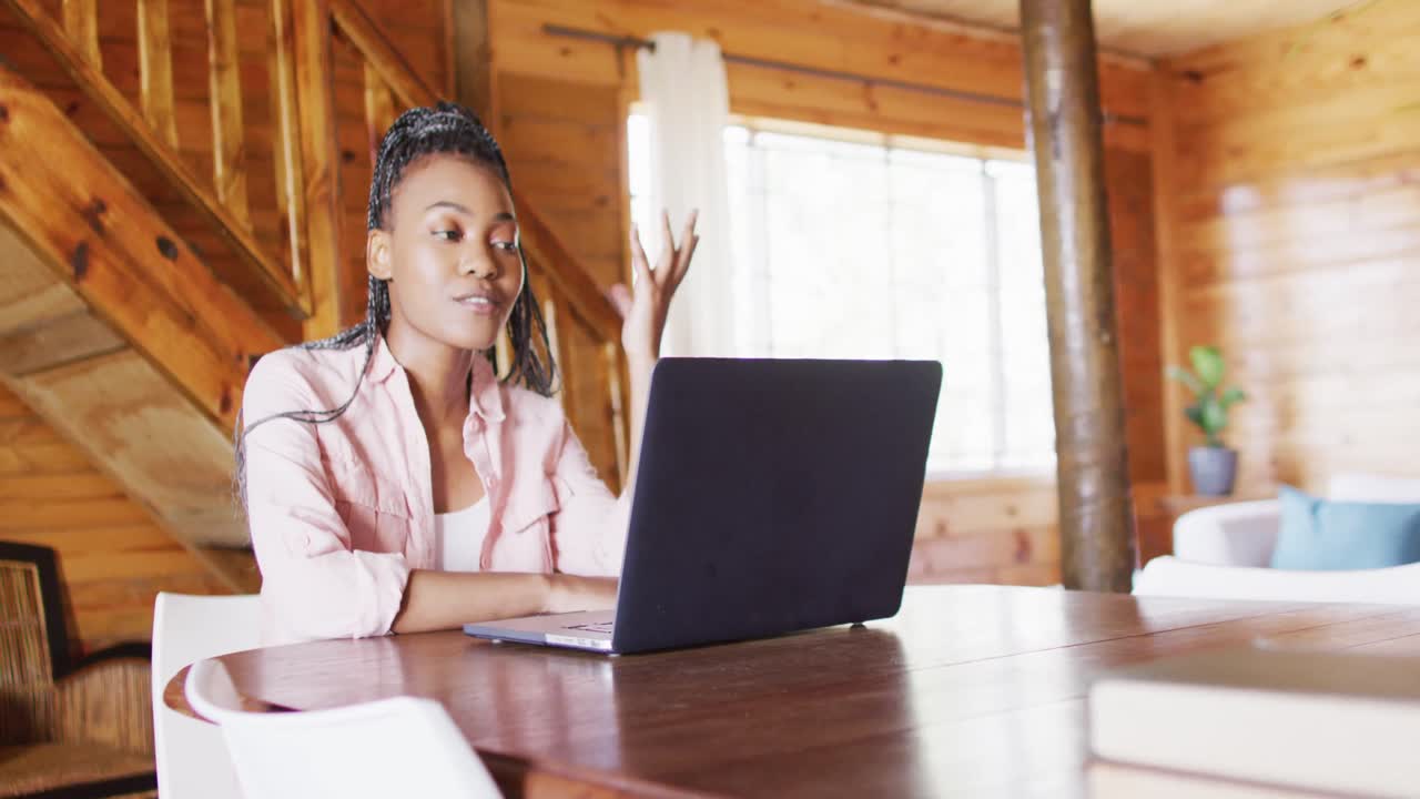 Glückliche afroamerikanische Frau sitzt am Tisch und nutzt einen Laptop für einen Videoanruf in Zeitlupe.