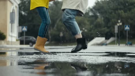 Close-up-of-a-woman-in-a-white-jacket-jumping-in-a-puddle-with-her-daughter-during-a-walk-in-the-park-after-the-rain