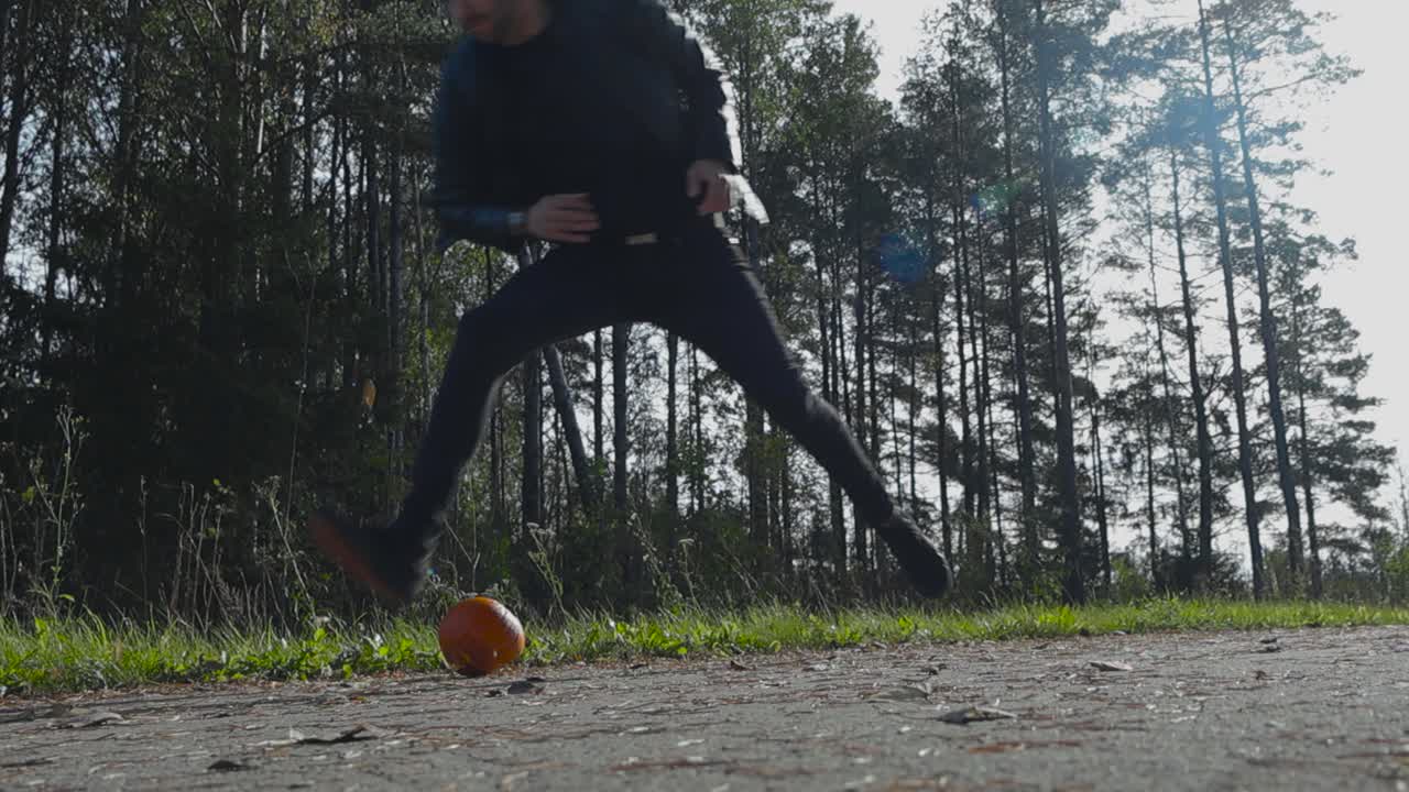 Person or a man throwing a Halloween pumpkin to the ground and destroying, smashing it in slow motion during autumn or late summer during holidays.Day time with cloudy weather and trees in the back.