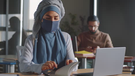 businesswoman in hijab and mask using laptop and taking notes