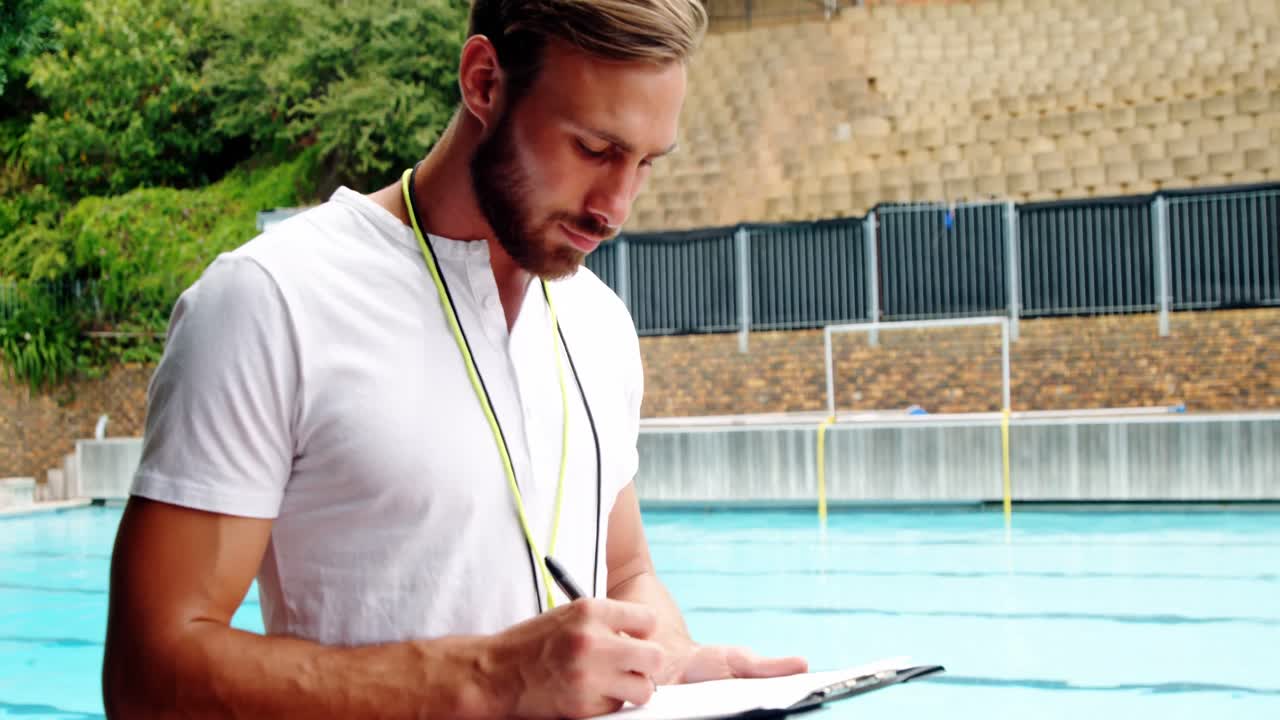 entrenador de natación escribiendo en el clipboard cerca de la piscina