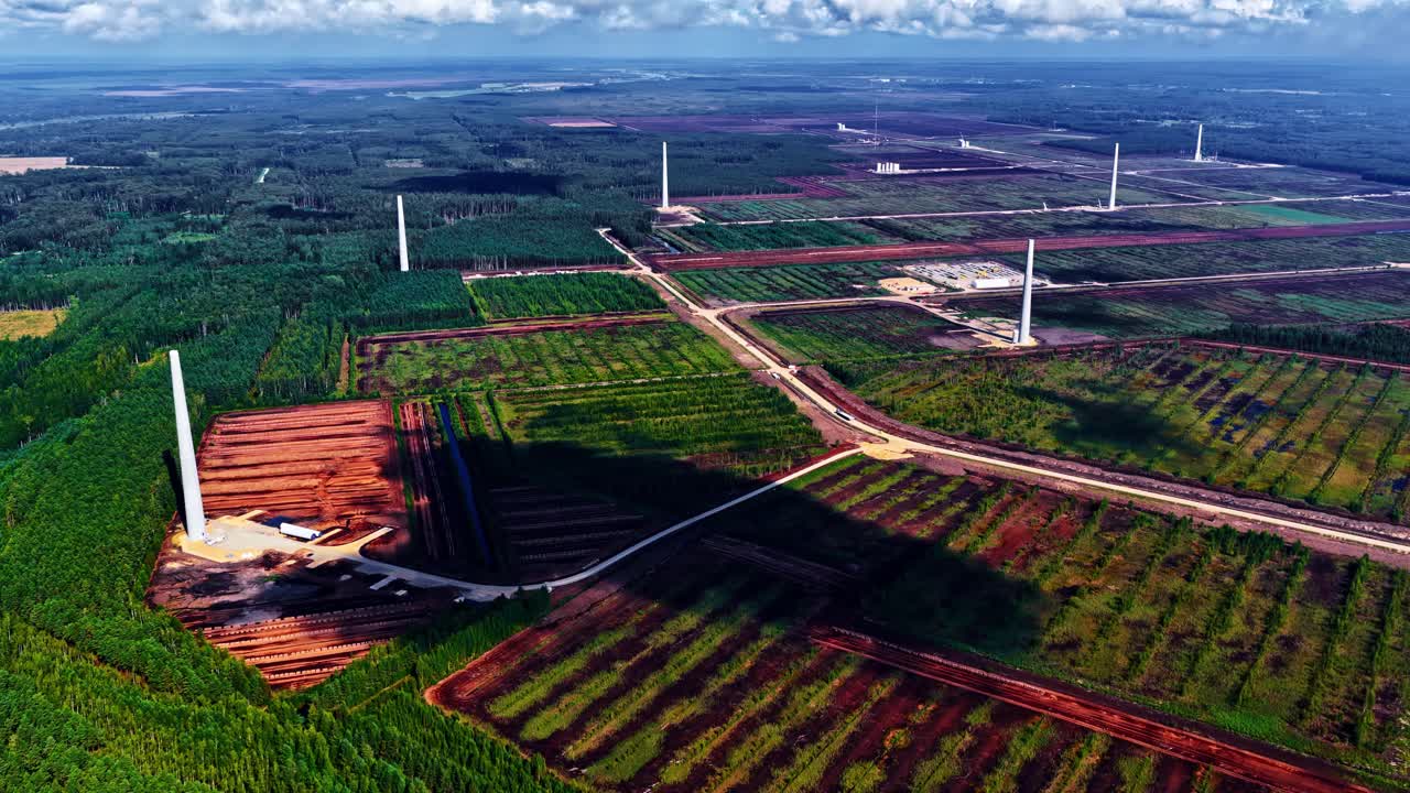 Top down drone shot of renewable energy site showing white turbine towers among summer woods and agricultural farmland in Latvia
