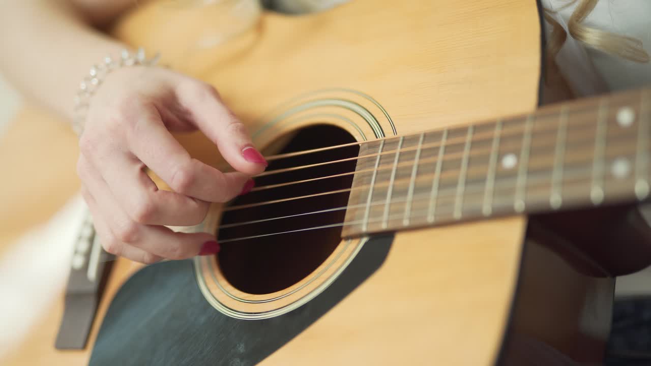 vista cercana de la mano de la mujer con manicura roja tocando la guitarra acústica clásica