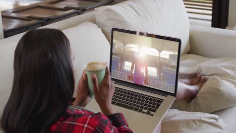 compuesto de una mujer sentada en casa sosteniendo café viendo un evento deportivo en una computadora portátil