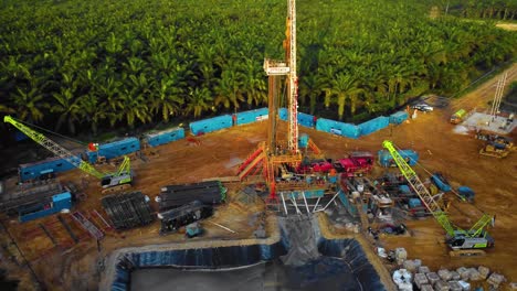 cinematic 4k drone footage of onshore drilling rig equipment structure for oil exploration and exploitation in the middle of jungle surrounded by palm oil trees during sunset and high oil price