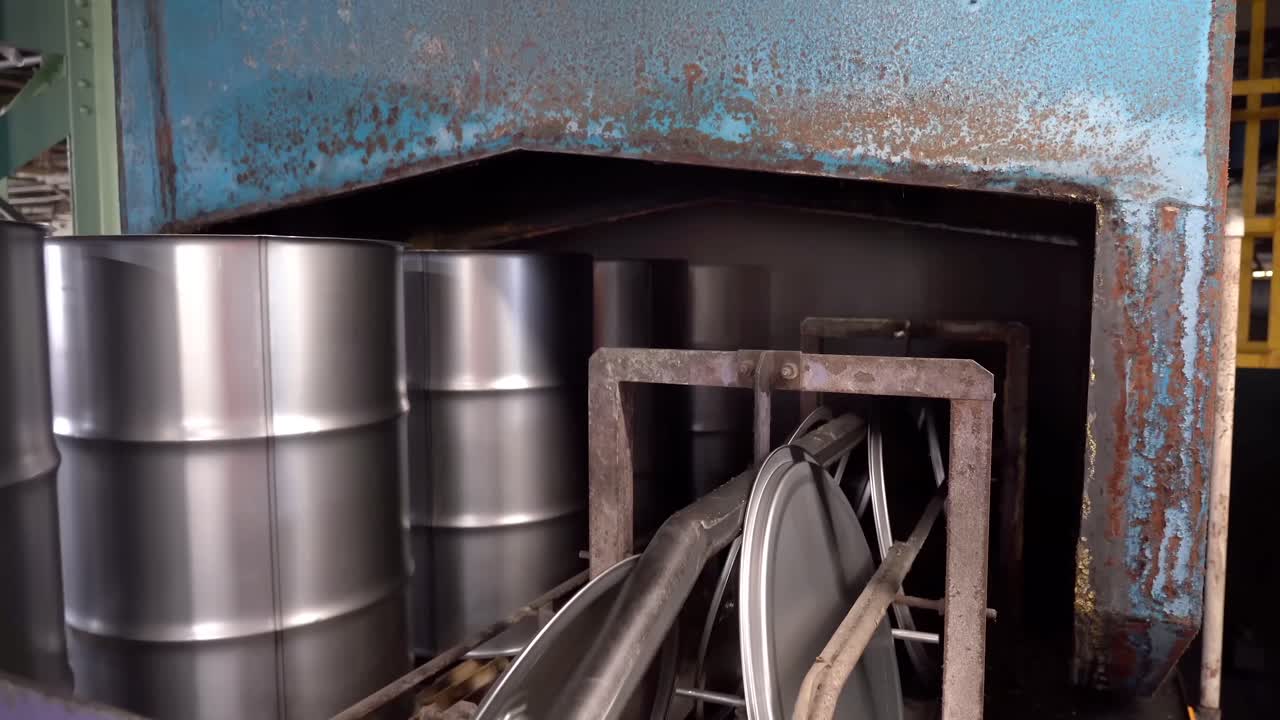 A conveyor belt carries steel drum cans and lids along the production line