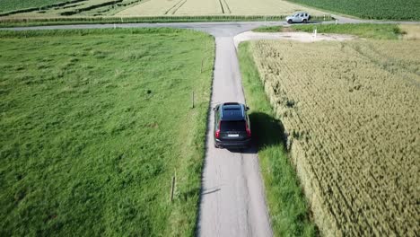 a large volvo xc90 4x4 car drives through the fields of the swiss countryside and approaches an intersection with another road